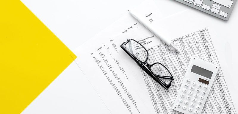 Glasses, calculator, and pencil on top of personal finance documents near a keyboard
