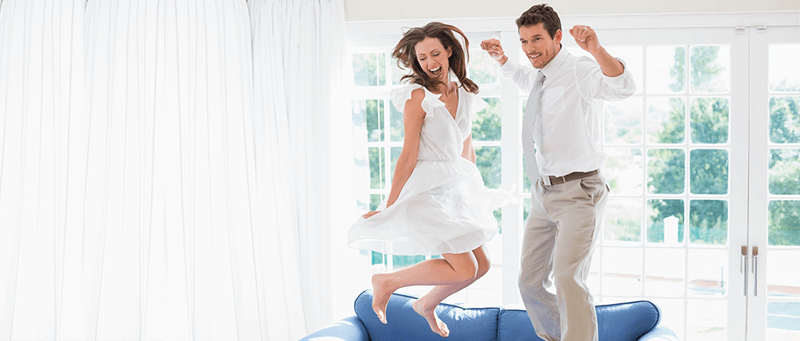 Happy couple jumping on couch in new home
