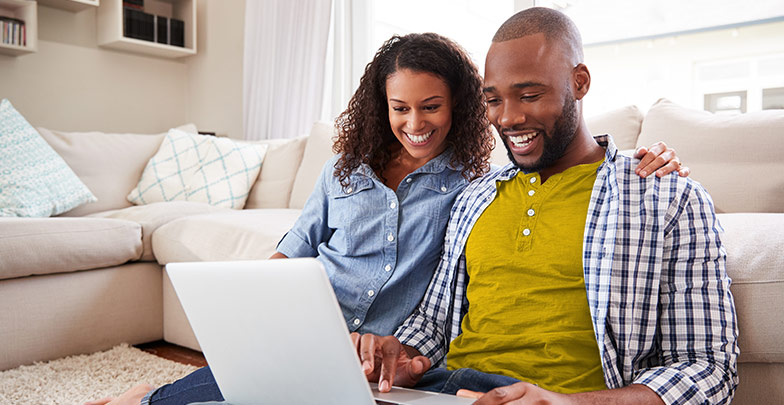 Couple at home in living room looking at options together on a a laptop