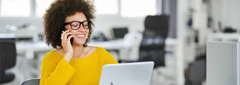 Young smiling woman looking at loan options on laptop while talking on phone