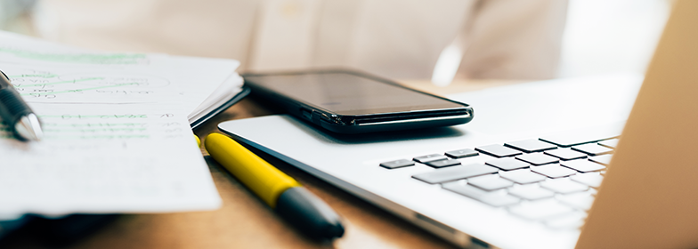 Laptop, cell phone, paper and pen on desk