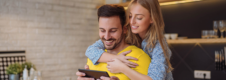 A couple hugging while both looking at a tablet