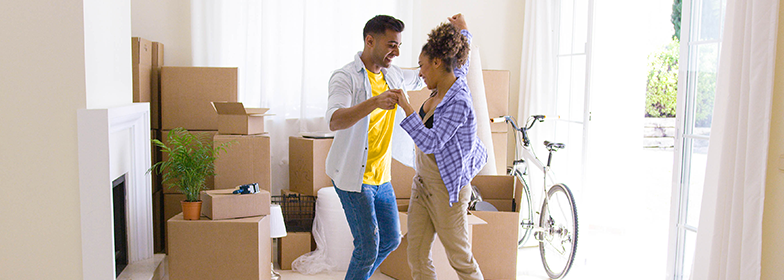 A couple dancing in their living room surrounded by moving boxes