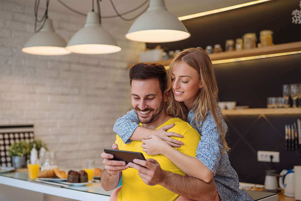 photo landscape young couple in kitchen looking at smartphone-edited (1) Happy couple looking at tablet
