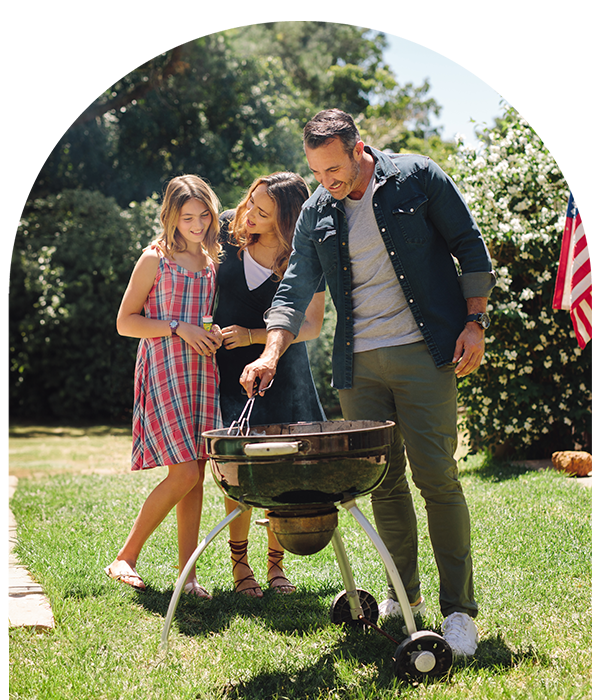 Smiling family around a grill in backyard