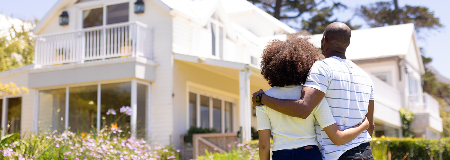 Couple standing with their arms around each others' shoulders looking at new home